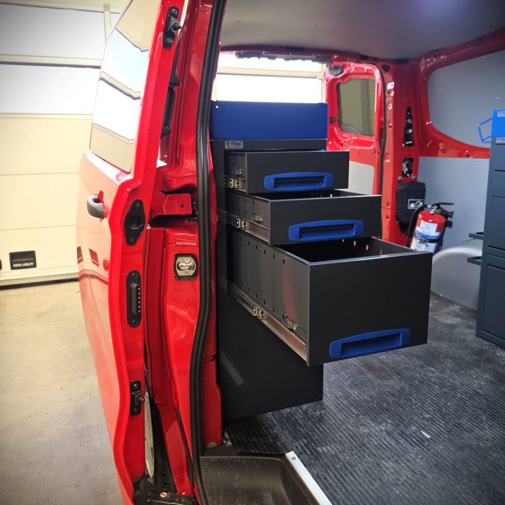 Ford Transit Custom L1 als Servicefahrzeug für einen Elektriker der Feuerwehr, ausgestattet mit einem 100 cm breiten und 96 cm hohen E-Flex Regalsystem auf der rechten Fahrzeugseite, bequem zugänglich durch die Schiebetür.
